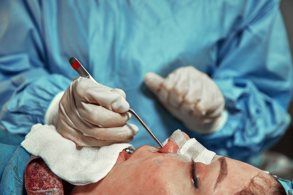 A surgeon with gloves is operating on his nose. Rhinoplasty, close-up operation. Blue light