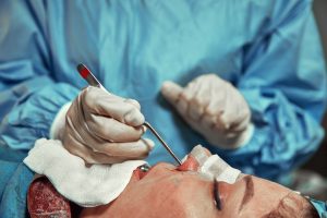 A surgeon with gloves is operating on his nose. Rhinoplasty, close-up operation. Blue light