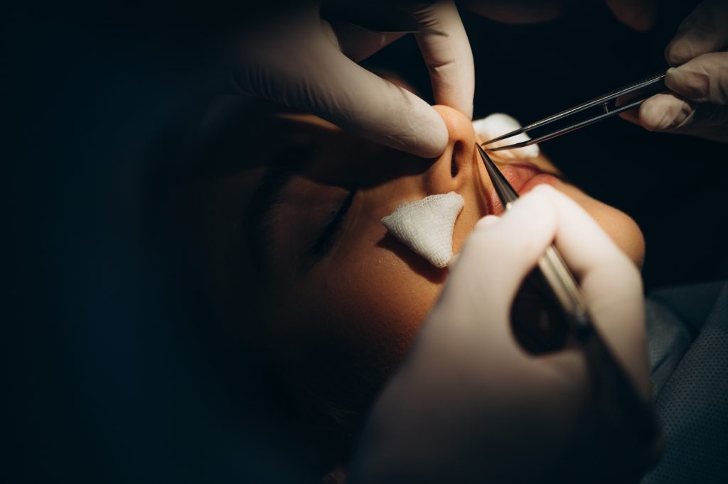 Surgeon and his assistant performing cosmetic surgery on nose in hospital operating room.